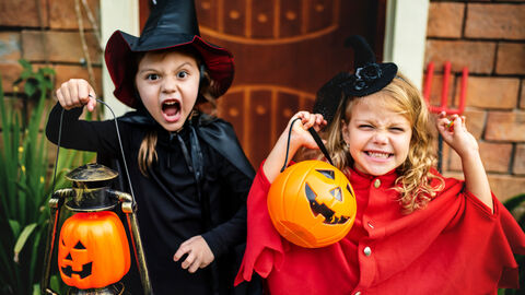 Zwei Kinder in Halloweenkostümen machen Gruselposen und lachen.