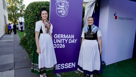 Zwei Frauen in Tracht stehen neben einem Aufsteller "German Unity Day 2026"